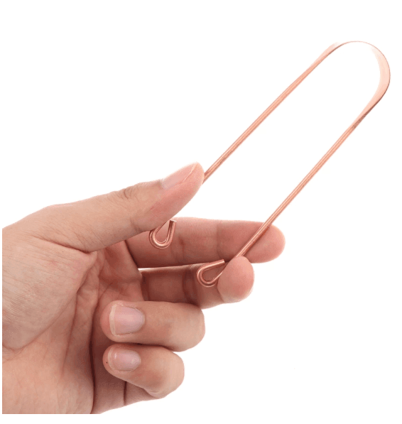 a hand holding a copper tongue scraper